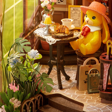 Ein Kaninchen mit Hut sitzt an einem gedeckten Tisch auf der Terrasse des Robotime Holiday Café