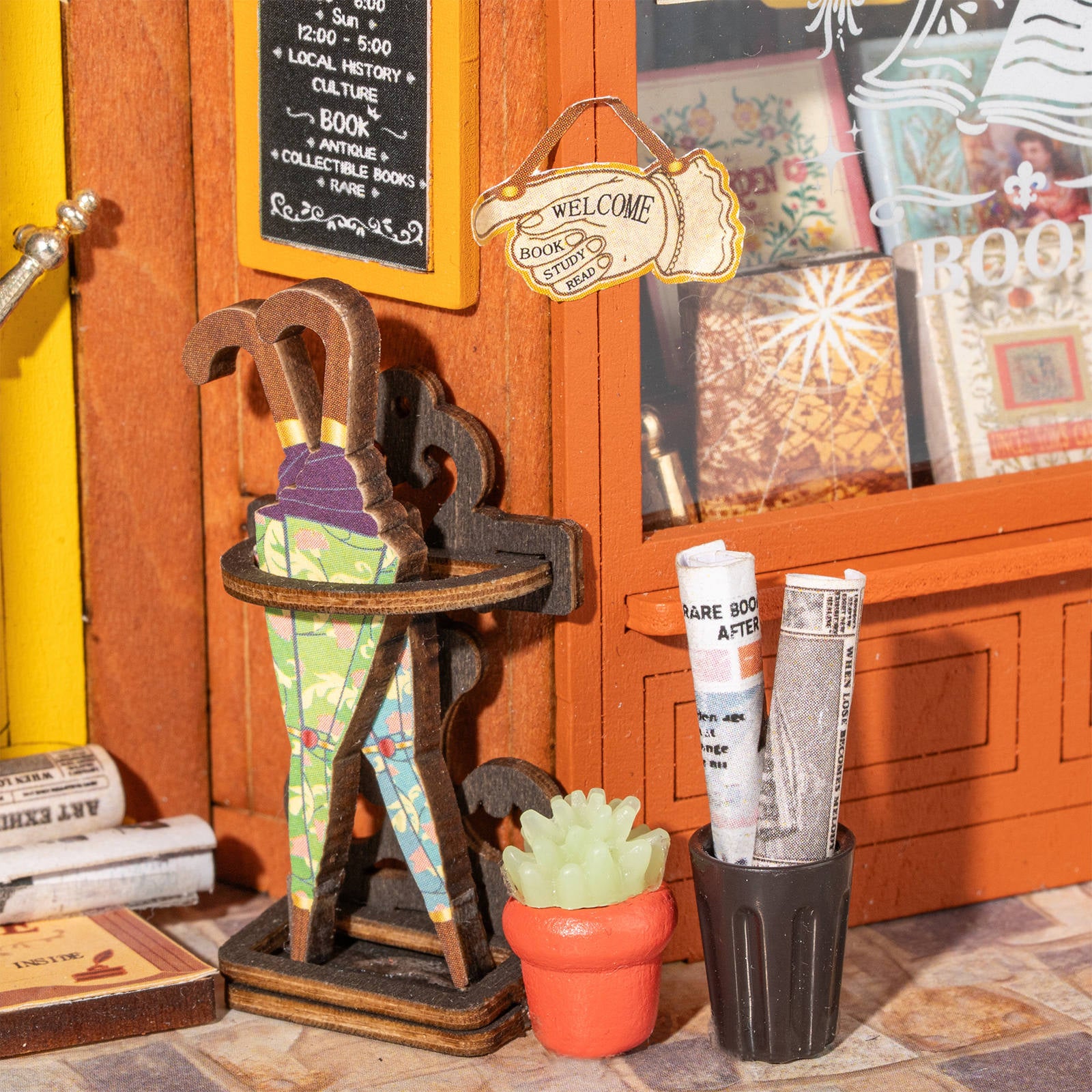 Schirmständer, Willkommensschild, Pflanze und Zeitungen am Eingang des Robotime Old Time Bookstore