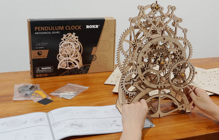 Atmosphärenfoto der fertigen Robotime Pendulum Clock mit Verpackungsinhalt und Verpackung im Hintergrund