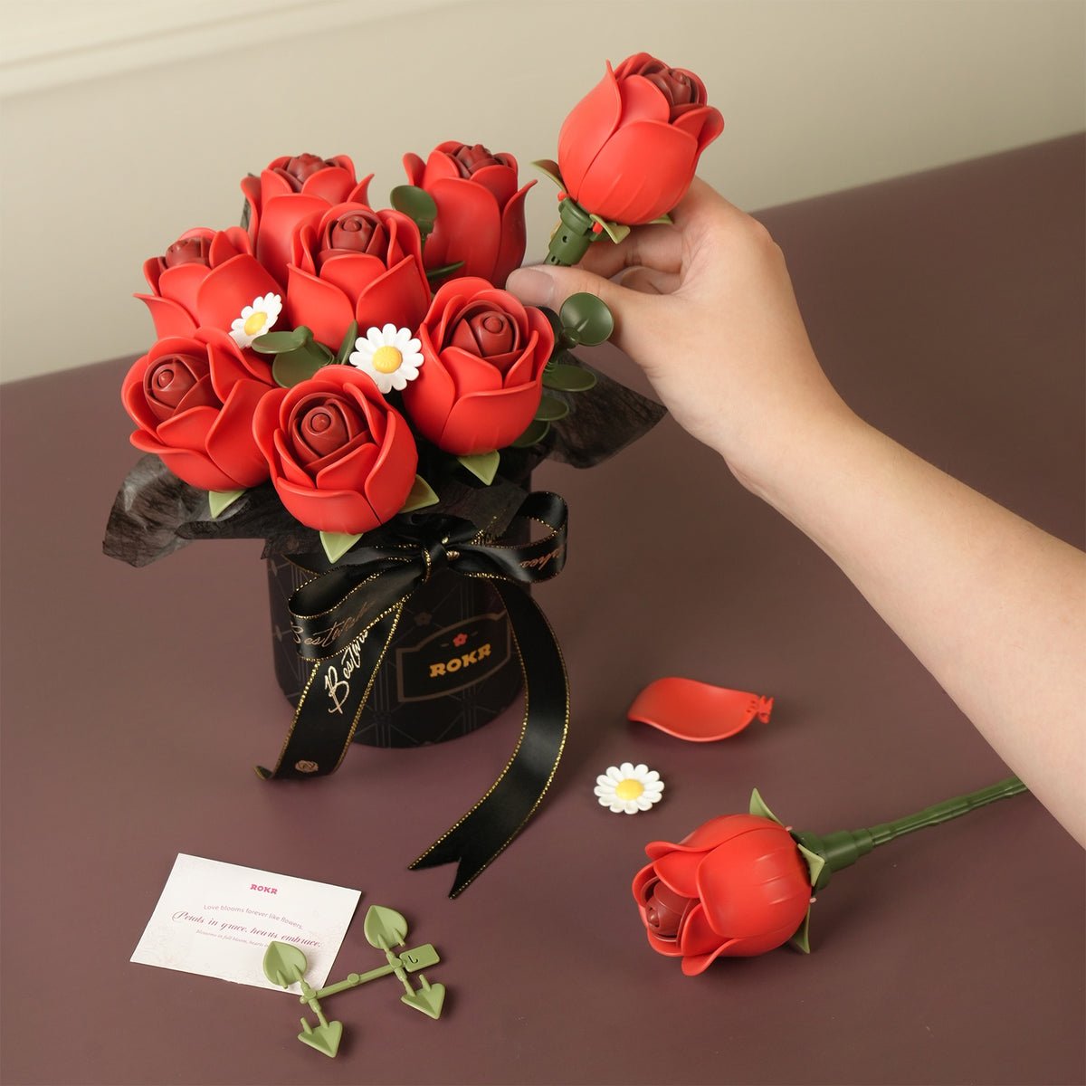Eine Person stellt gebastelte Rosen in die Vase des Robotime Red Rose Bouquet